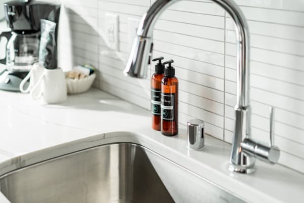 Kitchen countertop featuring a stainless steel sink, chrome faucet, amber soap bottles, and a coffee maker.