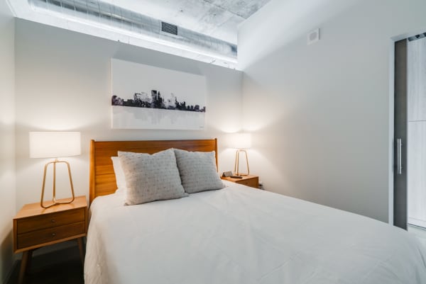 A modern bedroom with a white bed, wooden headboard, soft pillows, and lamps on either side.