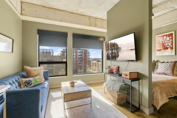 A modern living space featuring a blue sofa, coffee table, and mounted TV, with a cozy bed in the background.