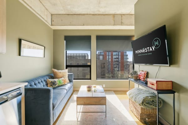 Modern living space with a blue sofa, wooden coffee table, and urban view through large windows.