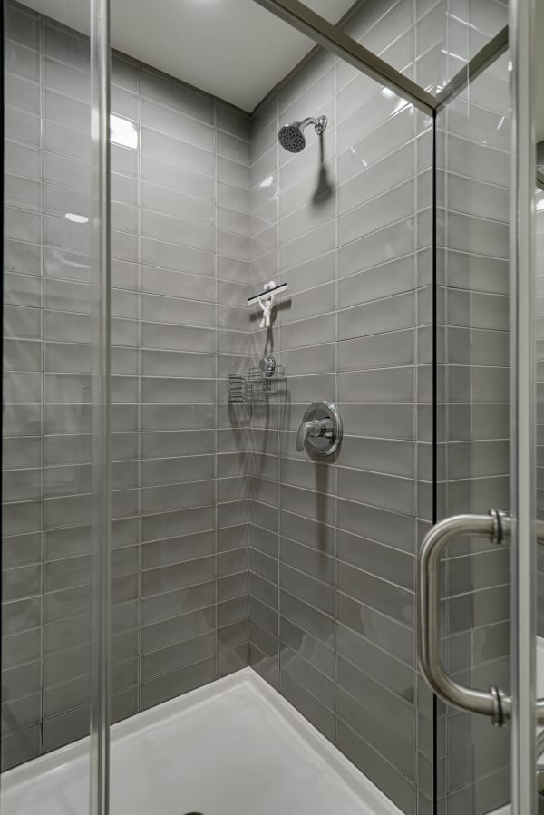 Modern shower with grey tiles, a chrome showerhead, and a whimsical cleaning figure.