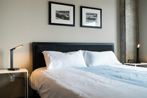 A modern bedroom featuring a neatly made bed, bedside lamps, and framed racing photographs.