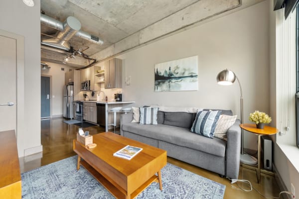 Modern living room with a gray sofa, wooden coffee table, and open kitchen.