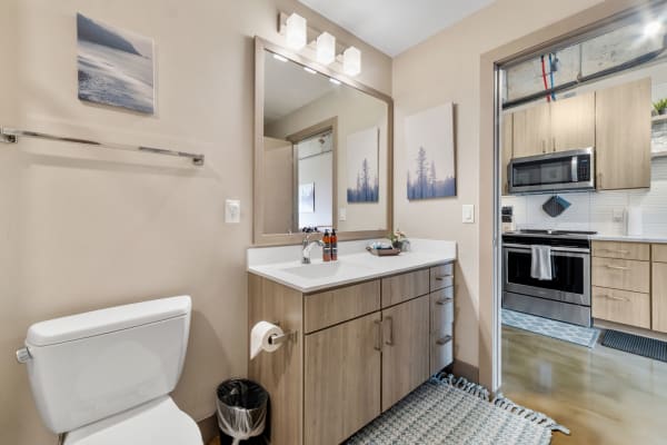 A minimalist bathroom featuring a light wood vanity, modern sink, and adjoining kitchen view.