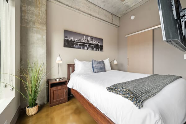 A modern bedroom featuring a concrete wall, large window, and a neatly made bed with decorative elements.