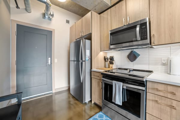 A contemporary kitchen with light wood cabinets, stainless steel appliances, and polished concrete floor.