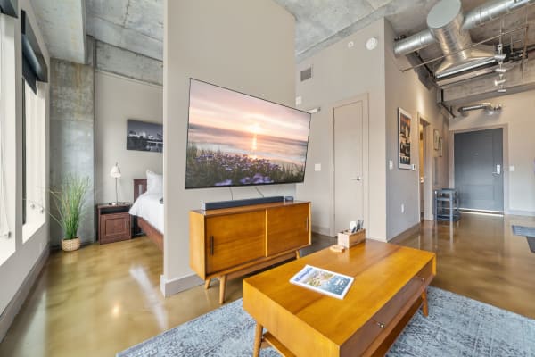 A contemporary living room with a flat-screen TV, stylish furniture, and an industrial ceiling.