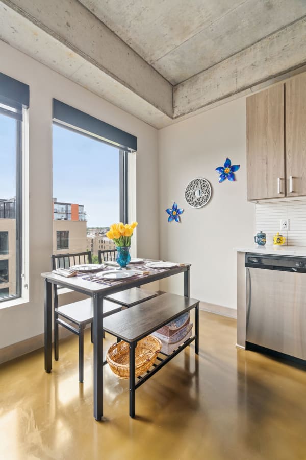 Modern kitchen nook with a dining table set for a meal, featuring yellow tulips in a blue vase and contemporary decor.