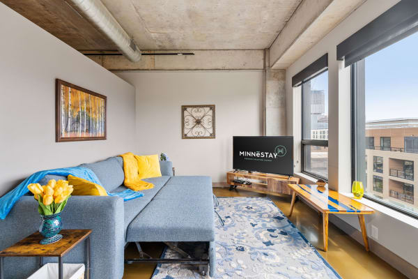 Modern living room with blue sectional sofa, bright pillows, and large windows.