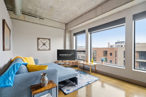 Cozy living room with a blue couch, yellow throw, and city view through large windows.