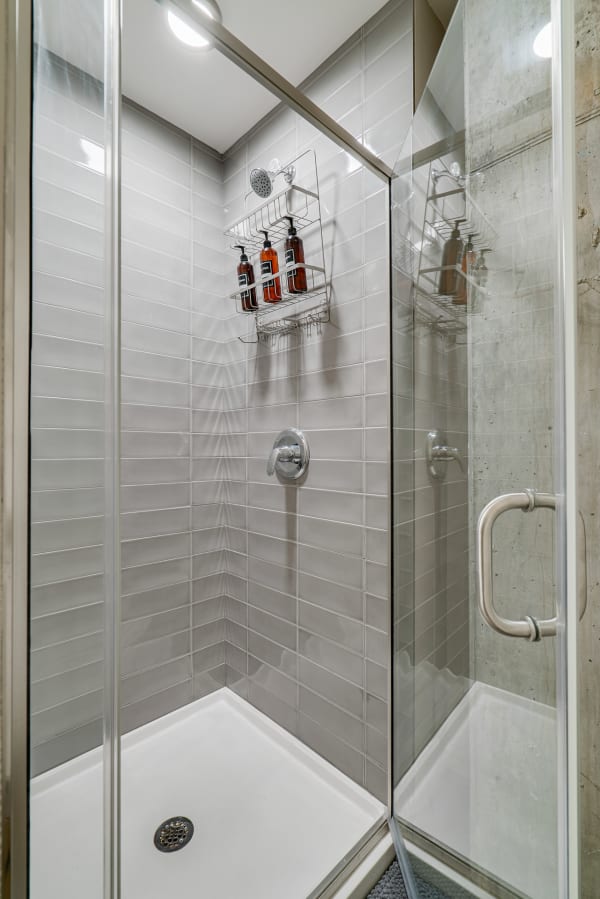 A sleek and modern shower space featuring gray tiles and glass doors with a product shelf.