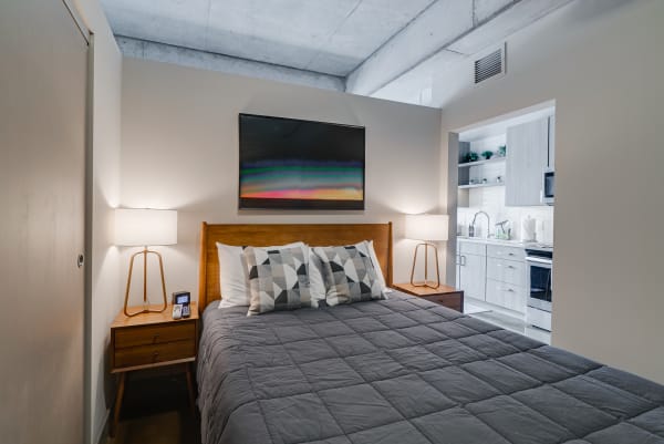 A cozy modern bedroom with a bed, geometric pillows, nightstands, and a view of a kitchen.