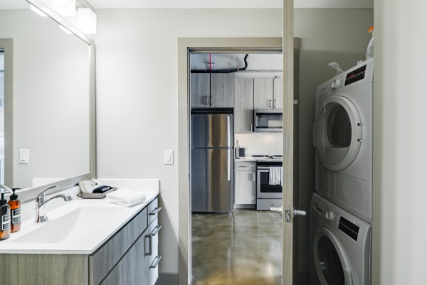 A contemporary bathroom with a view into a kitchen and laundry area beyond.