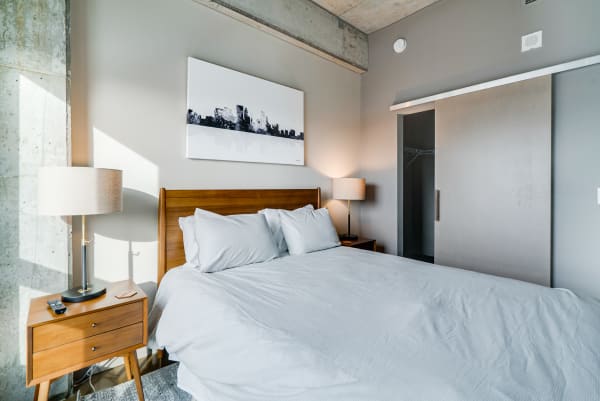 A contemporary bedroom featuring a bed, nightstand, lamp, and abstract skyline art.