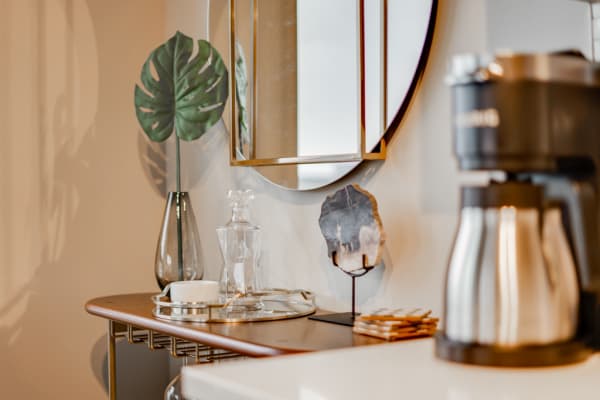 Contemporary coffee station with decorative elements including a coffee maker, a vase with a monstera leaf, and a mirror.