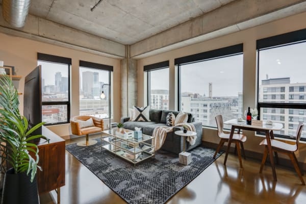 A contemporary apartment living room featuring large windows, a gray couch, and a stylish dining area.