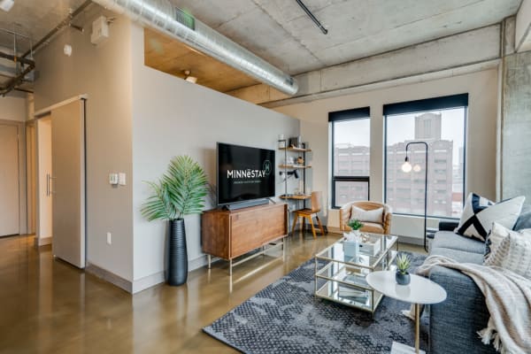 A modern living room featuring a gray sofa, stylish decor, and large windows with an urban view.