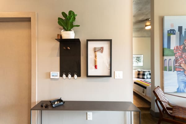 Entryway with modern decor featuring an axe in a frame, a potted plant, and a black table holding sunglasses.