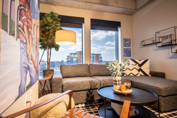 Modern living room with a gray sofa, artistic wall mural, and city view through windows.