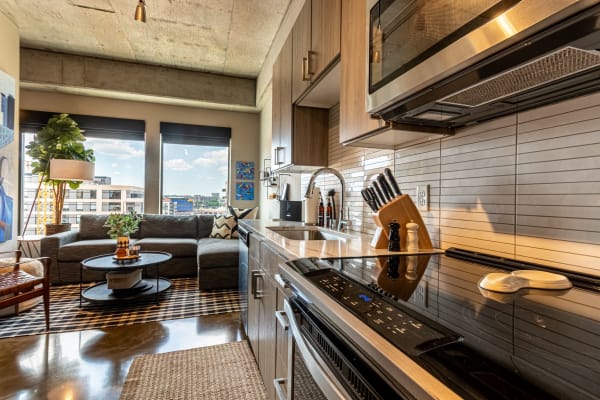 A contemporary kitchen and living room interior showcasing a gray sofa, black stovetop, and city view windows.