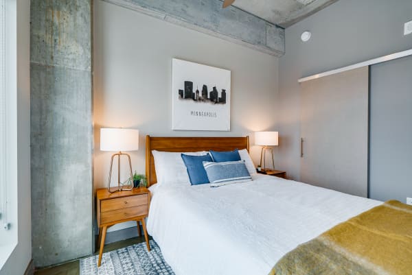 Modern bedroom with a white bed, blue pillows, wooden nightstands, and Minneapolis skyline art.