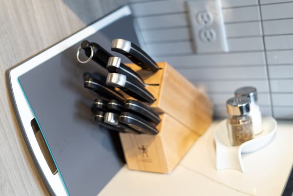 A knife block with black handles, a gray cutting board, and salt and pepper shakers on a white dish on a countertop.