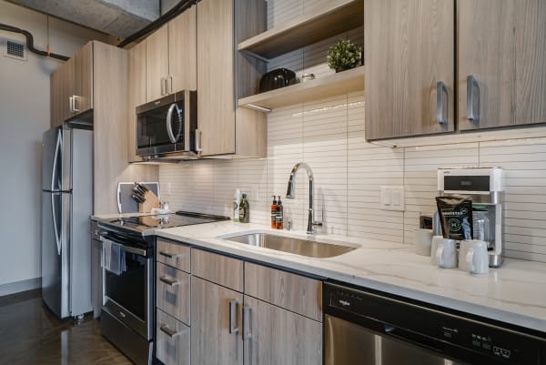 Contemporary kitchen with light wood cabinets, marble countertop, and stainless steel appliances.