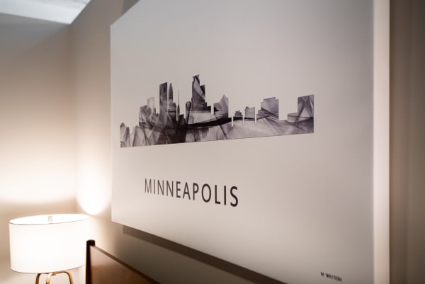 Artistic representation of Minneapolis skyline in black and white, with a lamp and bed in view.