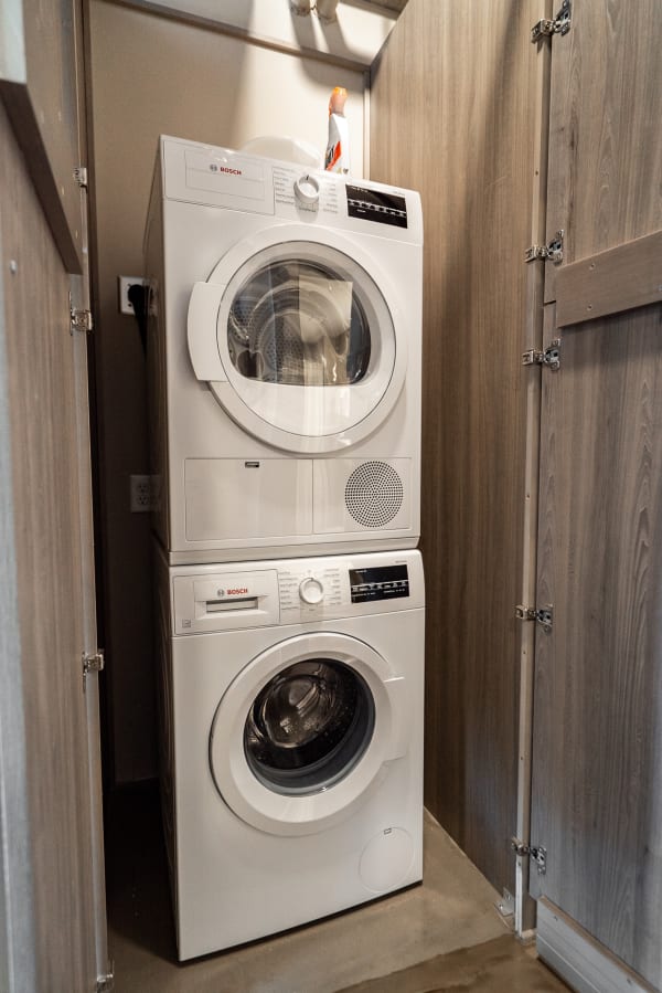 Stacked Bosch washer and dryer in a small laundry space with wooden cabinet backdrop.
