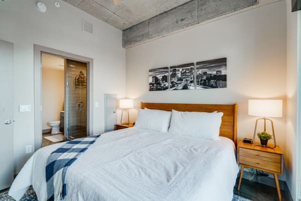 Contemporary bedroom with a wooden bed, black and white cityscape artworks, and a bathroom door.