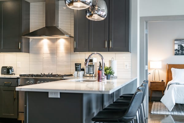 Modern kitchen with dark cabinets, a white countertop, and stylish bar stools.