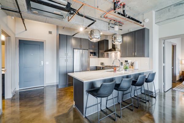 Contemporary kitchen featuring gray cabinets, a large island with black bar stools, and stainless steel appliances.
