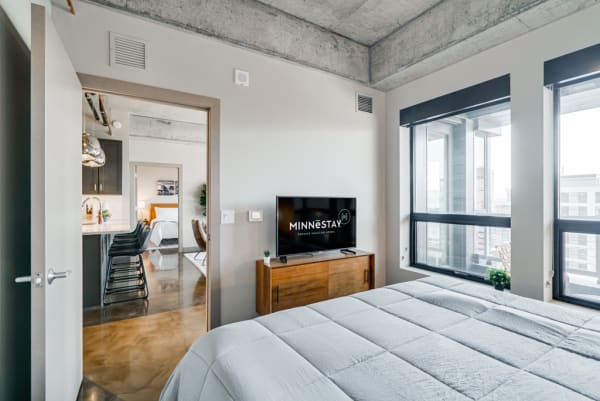 Cozy contemporary bedroom with television, bed, and views of the city.