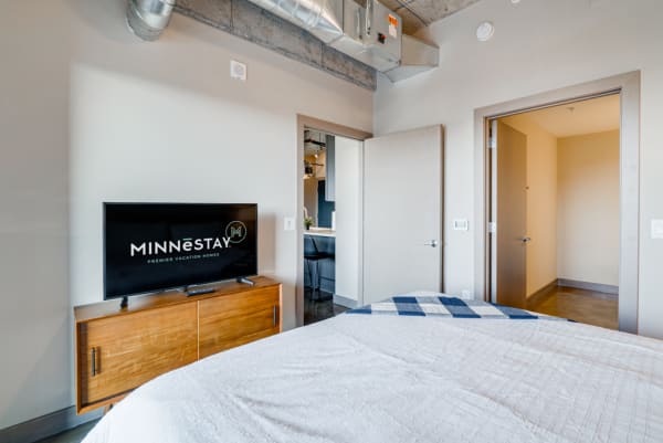 Interior view of a modern bedroom featuring a bed, a wooden dresser, and a television.