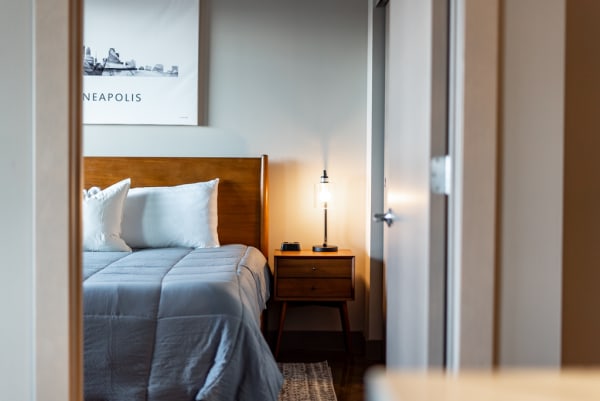 A view of a cozy modern bedroom with a wooden bed, nightstand with lamp, and artwork of Minneapolis.