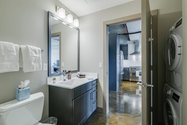 A modern bathroom with a dark vanity, a large mirror, and a view into a stylish kitchen area.