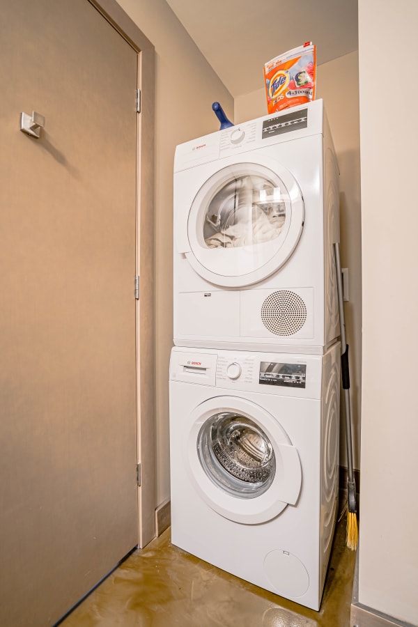 Stacked washer and dryer with laundry detergent on top in a small laundry space.