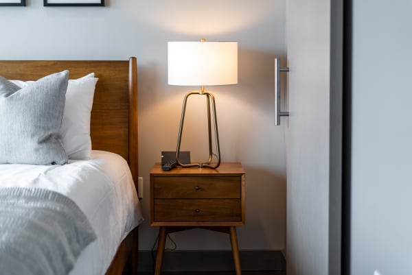 A cozy bedroom with a wooden bed, a wooden nightstand with a lamp, and a modern door handle.