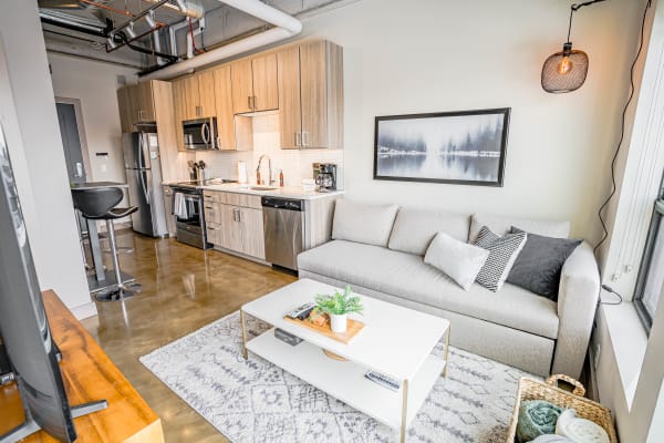 Modern studio apartment with kitchen and living area featuring a sectional sofa and natural light.