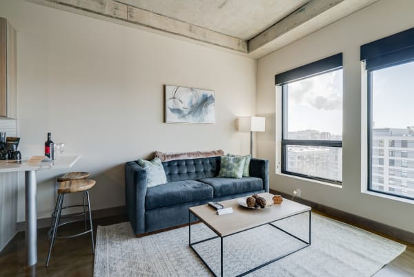 A modern living space featuring a blue velvet sofa, abstract artwork, and cityscape views through large windows.