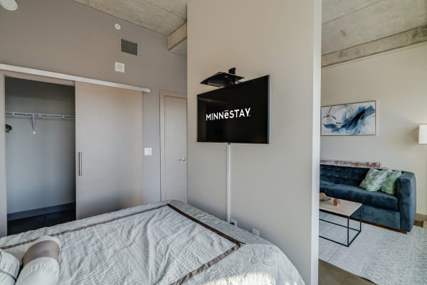 Modern bedroom with a neatly made bed, wall-mounted TV, and blue sofa.