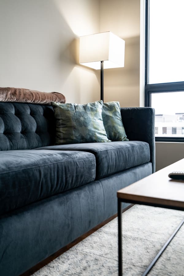 A dark blue tufted sofa with green patterned pillows and a nearby lamp.