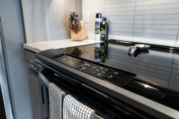A black electric stove with digital controls and a kitchen towel on the handle in a contemporary kitchen.