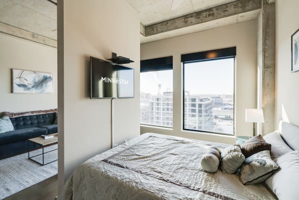 Stylish bedroom corner with a bed, decorative pillows, city view, and mounted television.