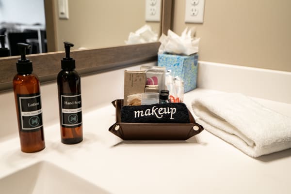 Bathroom countertop featuring lotion, hand soap, a makeup tray, and a folded towel.
