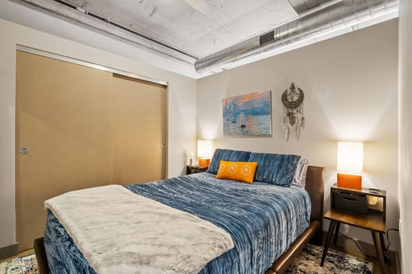 A modern bedroom featuring a blue bedspread, artwork on the wall, and stylish decor.