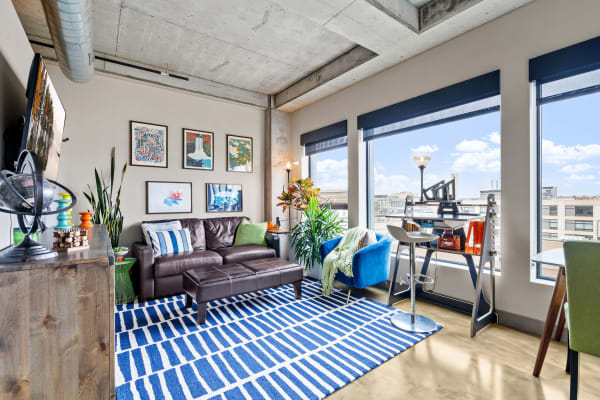 Modern living room with a leather couch, artwork on the walls, and a workspace near the windows.