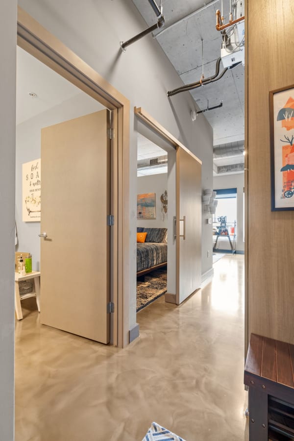 A well-lit apartment hallway with a polished concrete floor and an open bedroom door, showcasing modern decor.
