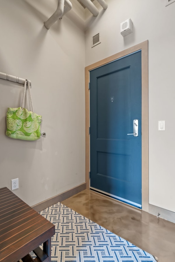 A minimalist entryway with a blue front door, dark wooden bench, green bag, and patterned rug.