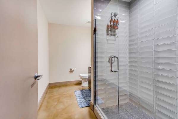 A contemporary bathroom with a glass shower, toilet, and a blue bath mat on a polished concrete floor.